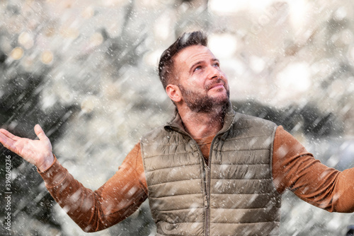 Handsome smiling man standing outside and enjoy snowing fall. Portrait shot of young guy standing outside while falling snow. 