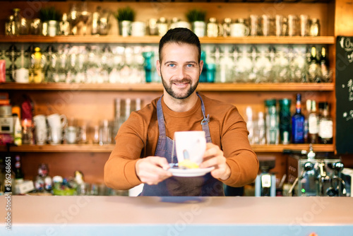 Smiling male coffee shop owner businessman standing behind the counter in the cafe and holding a cup of tea in his hand. Small business.