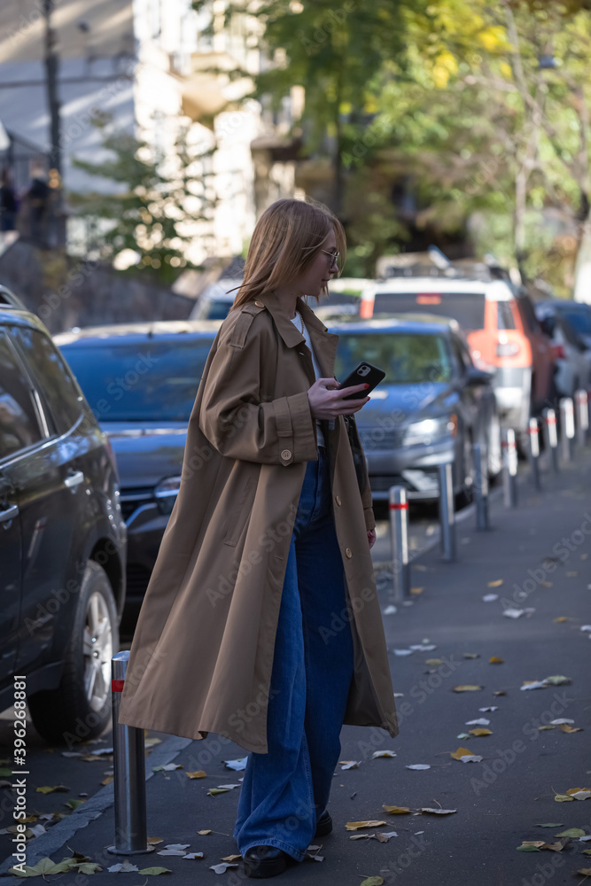 Young woman in a fashionable long coat walks in autumn city. copy space