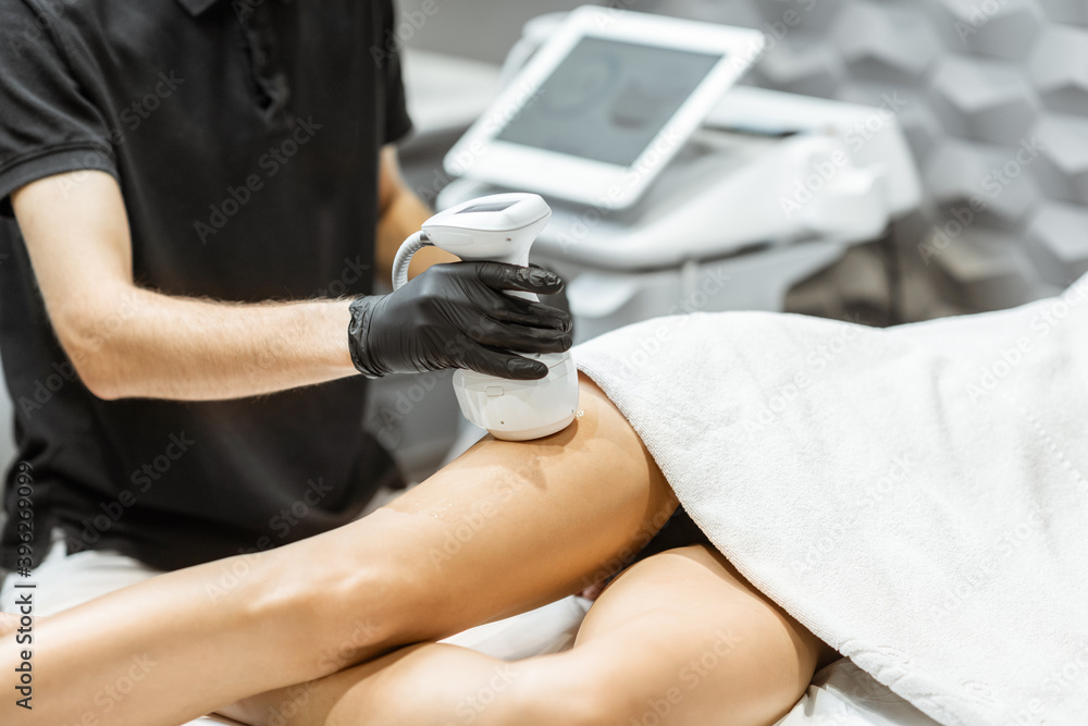 Young woman during an ultrasound liposuction procedure at luxury Spa salon. Doctor working on thigh area, close-up