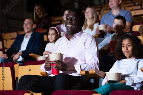 Portrait of cheerful laughing african american man sitting in movie theater with popcorn and watching comedy..