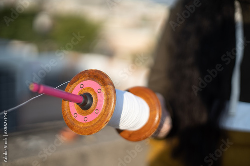 slow motion shot of thread being pulled quickly from charkhi spool as an out of focus person in the background flies the kite and takes the kite higher and farther photo