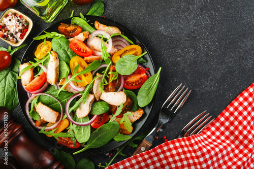 Fresh salad with spinach, chicken, tomatoes, arugula, corn lettuce and onion. Healthy food. Black table