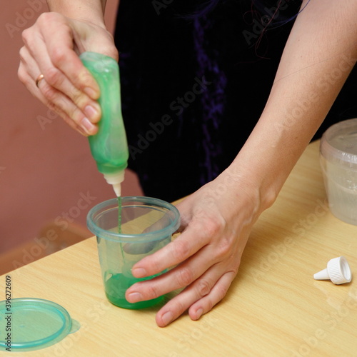 Slime toy in plastic cap on wooden table, woman white hands make slime game with base add hardener components mix, children's creativity indoor vacation