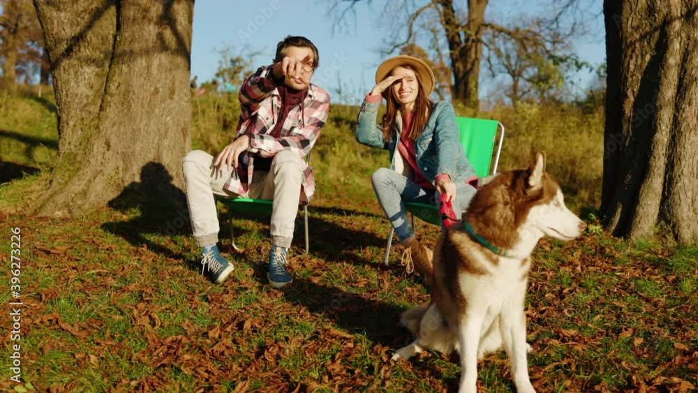 At sunlight happy smiling romantic lovely couple sitting with domestic pet dog in autumn park or forest. Animal relaxed portrait cheerful. Slow motion At sunlight happy smiling romantic lovely couple sitting with domestic pet dog in autumn park or forest. Animal relaxed portrait cheerful. Slow motion
