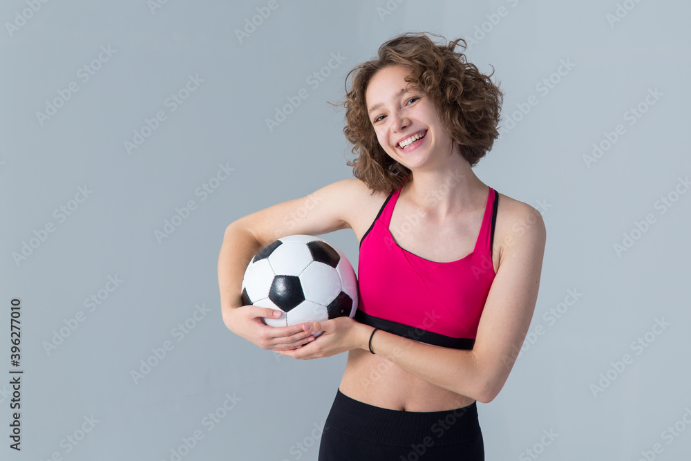 Sportive young woman with a soccer ball standing on a light gray background. Love football.