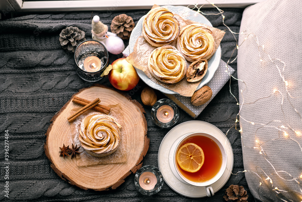 A cup of hot tea with lemon in an early winter morning by the window. Knitted wool warm blanket, hot homemade apple cakes with cinnamon and star anise . Decor. Home winter holiday concept. A cup of hot tea with lemon in an early winter morning by the window. Knitted wool warm blanket, hot homemade apple cakes with cinnamon and star anise . Decor. Home winter holiday concept.