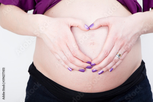 Pregnant women holding her hands heart shaped on her belly. Studio portrait isolated on white background. 