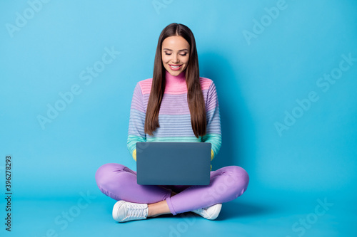 Portrait of lovely focused cheery girl sitting lotus position crossed legs using laptop isolated on bright blue color background © deagreez