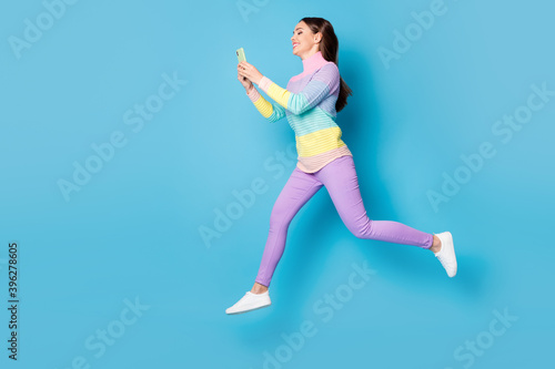 Full length body size view of nice focused cheery girl jumping using cell app 5g walking chatting isolated on bright blue color background