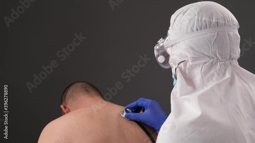 doctors in a protective suit examines a man with symptoms of coronavirus, the doctor listens to the sick breathing with a stethoscope. photo