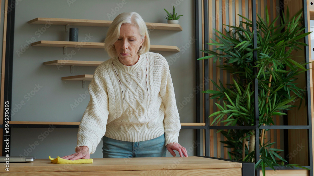 Elderly woman wipes her Desk with a rag. Concept of homework and household management Elderly woman wipes her Desk with a rag. Concept of homework and household management