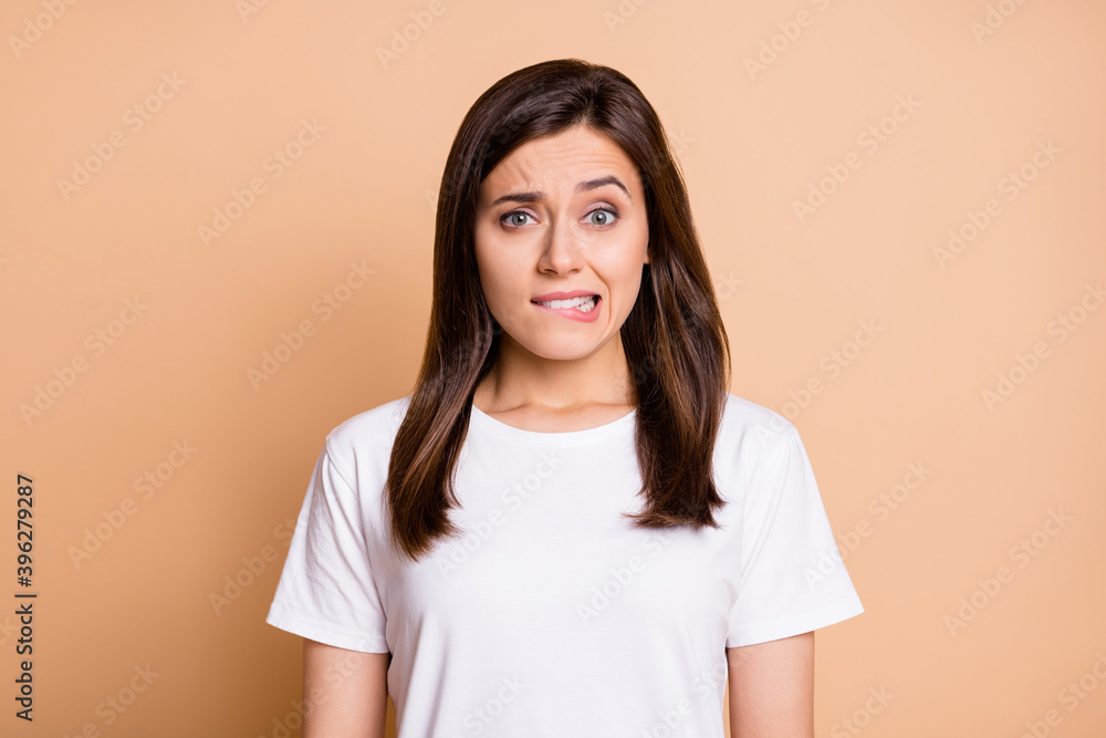Photo portrait of worried nervous young woman biting lip worried in casual clothes isolated pastel beige color background Photo portrait of worried nervous young woman biting lip worried in casual clothes isolated pastel beige color background