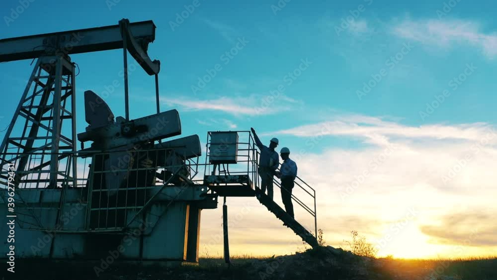 Two oil workers inspecting an oil field at bright sunset Two oil workers inspecting an oil field at bright sunset