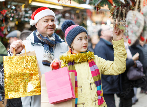 Young father with daughter having fun on Christmas fair, selecting decoration for home..