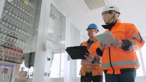 Mature engineer shows new cabinets with switchboards to female inspector checking modern wind power plant substation before start