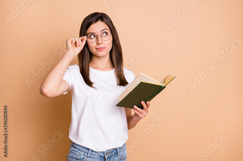 Photo portrait of clever female student in casual outfit keeping book looking blank space isolated pastel beige color background