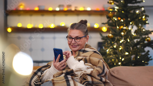 Senior woman sitting on sofa with smartphone at christmas time
