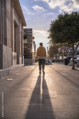 black afro american man with yellow sweatshirt turned back walking down city street with sun in background