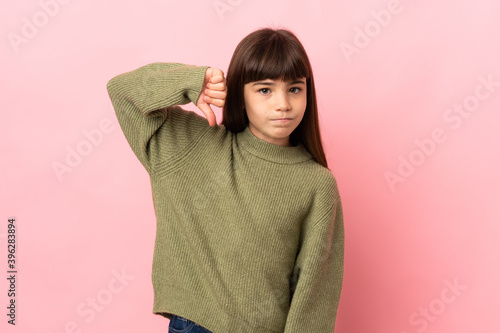 Little girl isolated on pink background showing thumb down with negative expression © luismolinero