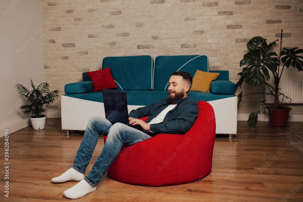 Pleasant and smiling bearded man looking at laptop screen and browsing funny movie.