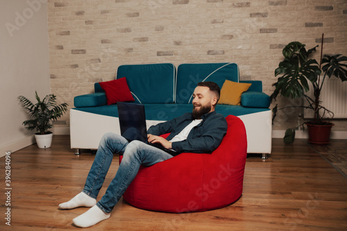 Obraz na płótnie Pleasant and smiling bearded man looking at laptop screen and browsing funny movie. w salonie