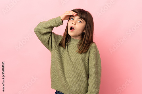 Little girl isolated on pink background doing surprise gesture while looking to the side
