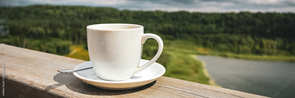 White cup of hot coffee on balcony with natural and mountains, hills background. Beverage, breakfast. White cup of hot coffee on balcony with natural and mountains, hills background. Beverage, breakfast.