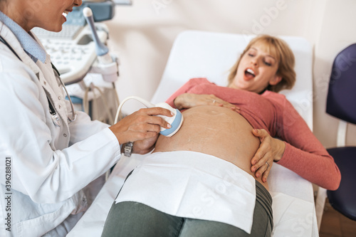 Beautiful and happy expectant mother at gynecological examination with ultrasound medical equipment.