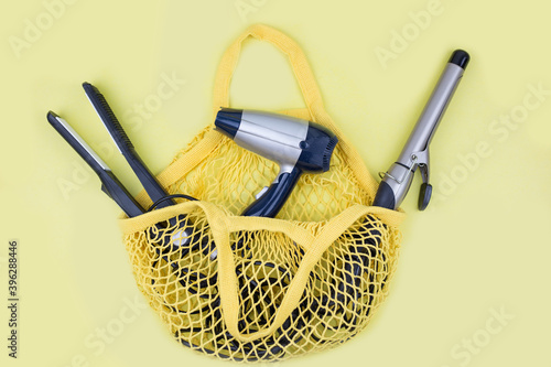 curling iron, hair dryer, straightener are in a yellow purse. Shopping bag with hairdresser items