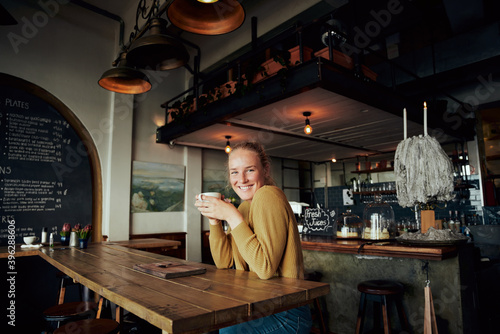 Portrait of young beautiful woman sitting in cafe leaning on table relaxing and holding coffee mug