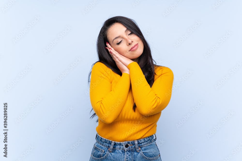 Young Colombian girl over isolated blue background making sleep gesture in dorable expression Young Colombian girl over isolated blue background making sleep gesture in dorable expression