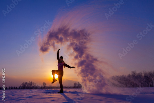 Silhouette of a sports girl at sunset in winter. Woman splashed boiling water on cold air.