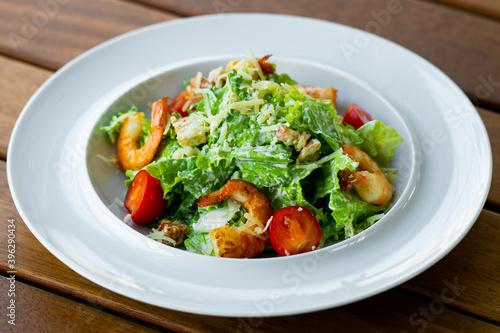 Delicious healthy caesar salad with shrimp in a white plate isolated on a wooden table.