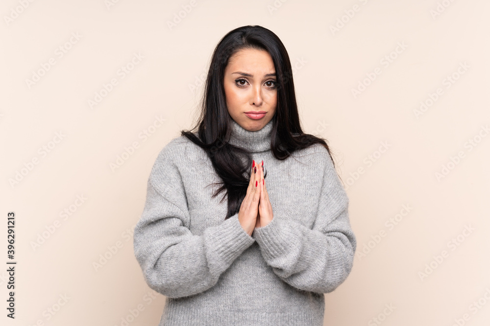 Young Colombian girl over isolated background keeps palm together. Person asks for something Young Colombian girl over isolated background keeps palm together. Person asks for something