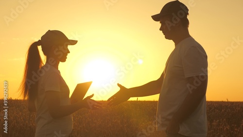 Farmer man and woman work with tablet in wheat field in sun. silhouette of agronomist and businessman with tablet examining wheat harvest in field. business people shaking hands. grain harvest