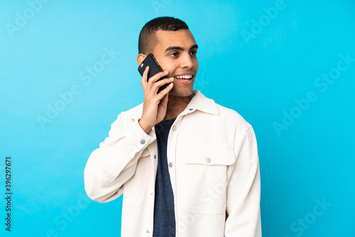 Young African American man over isolated blue background keeping a conversation with the mobile phone with someone