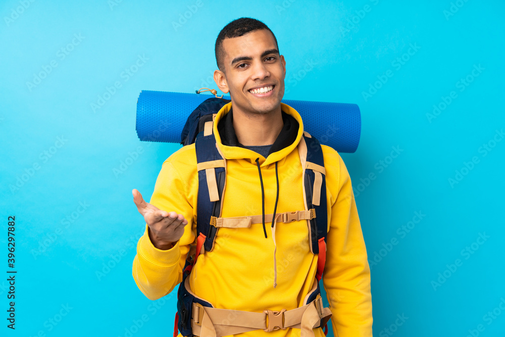 Young mountaineer man with a big backpack over isolated blue background handshaking after good deal Young mountaineer man with a big backpack over isolated blue background handshaking after good deal