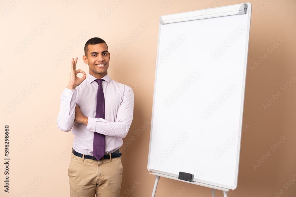 Young business man over isolated background giving a presentation on white board and showing ok sign with fingers Young business man over isolated background giving a presentation on white board and showing ok sign with fingers