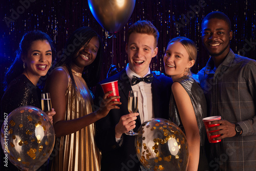 Waist up portrait of multi-ethnic group of friends smiling at camera happily while enjoying Birthday party or prom night photo