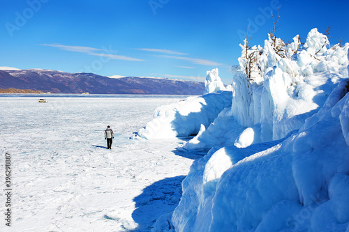 Beautiful winter landscape of Lake Baikal. A man walks on the frozen lake Baikal. Rocks and trees of Ogoy island covered with icicles and snow.