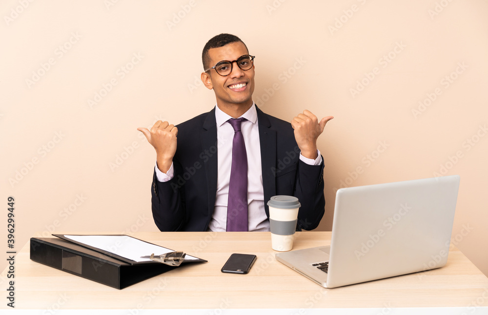Young business man in his office with a laptop and other documents with thumbs up gesture and smiling