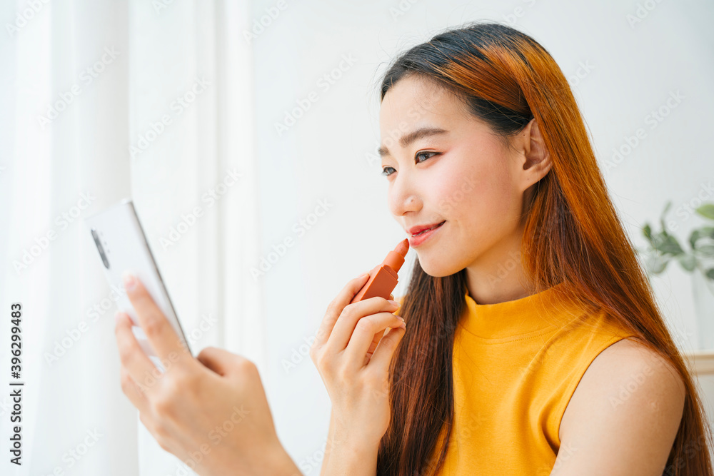Beautiful asian woman applying lipstick and looking at mirror on smartphone. Beautiful asian woman applying lipstick and looking at mirror on smartphone.