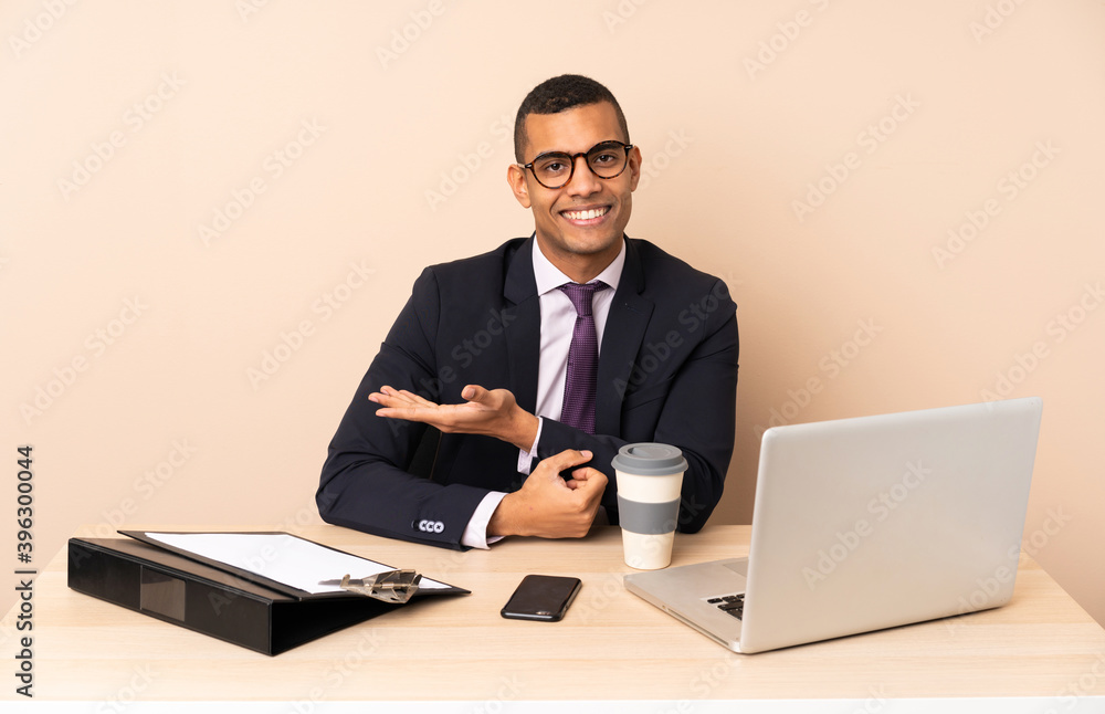 Young business man in his office with a laptop and other documents presenting an idea while looking smiling towards Young business man in his office with a laptop and other documents presenting an idea while looking smiling towards