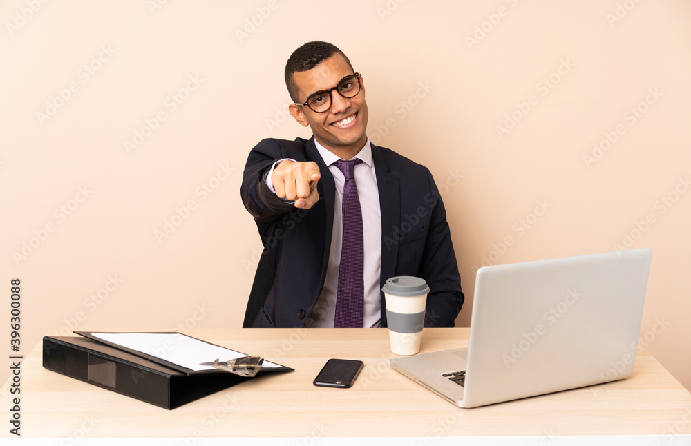 Young business man in his office with a laptop and other documents points finger at you with a confident expression Young business man in his office with a laptop and other documents points finger at you with a confident expression