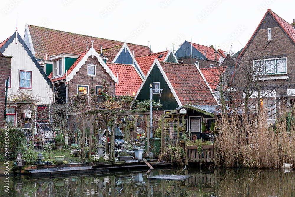 Dutch houses on water channel. A fishing village with vintage northern Netherlands houses with orange tile roofs. Backyard in front of pond. Volendam