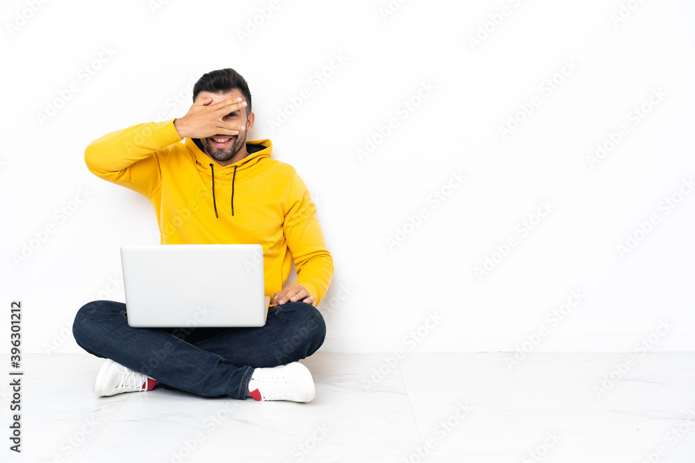 Caucasian man sitting on the floor with his laptop covering eyes by hands and smiling Caucasian man sitting on the floor with his laptop covering eyes by hands and smiling
