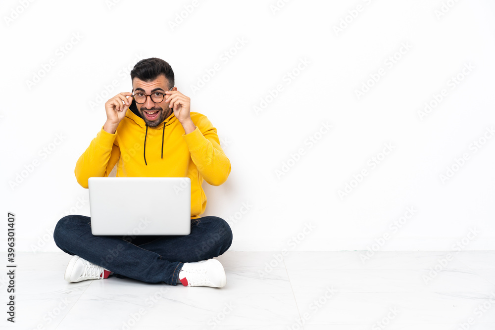 Caucasian man sitting on the floor with his laptop with glasses and surprised Caucasian man sitting on the floor with his laptop with glasses and surprised