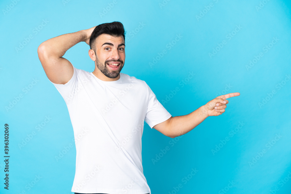 Caucasian man over isolated blue background surprised and pointing finger to the side Caucasian man over isolated blue background surprised and pointing finger to the side