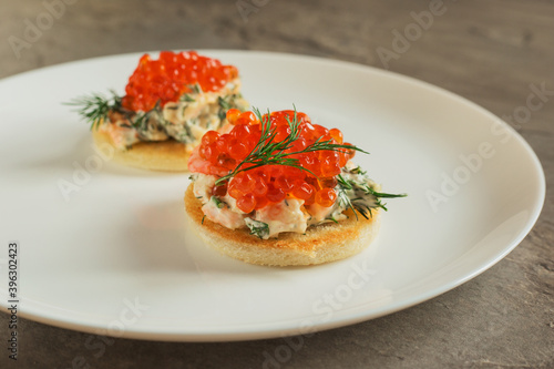 Toast skagen - classic Swedish appetizer. Sandwiches with shrimps and caviar on white plate. Selective focus.